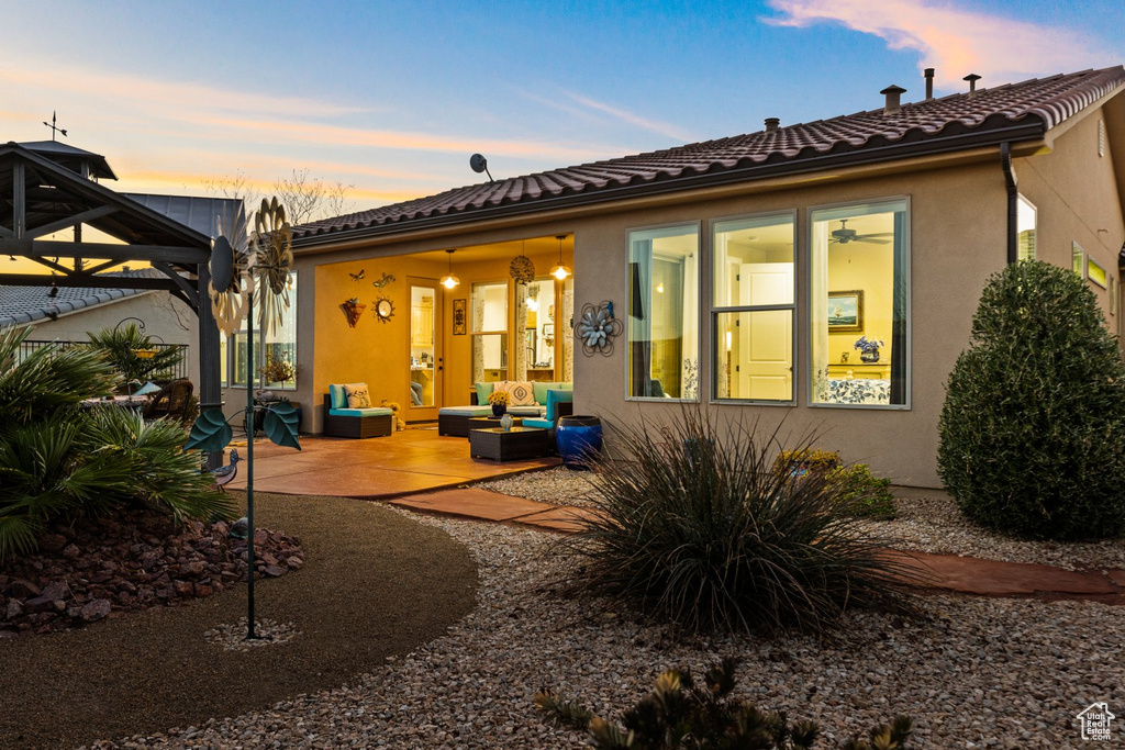 Back of property at dusk featuring stucco siding, a gazebo, a patio, and an outdoor hangout area