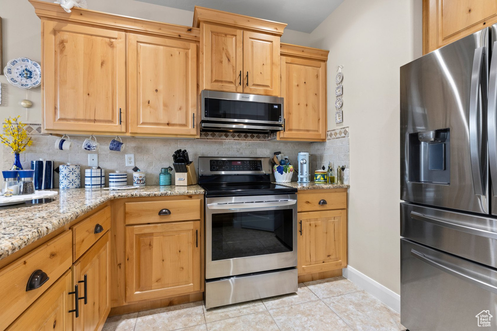Kitchen with light stone countertops, stainless steel appliances, decorative backsplash, light tile patterned floors, and baseboards