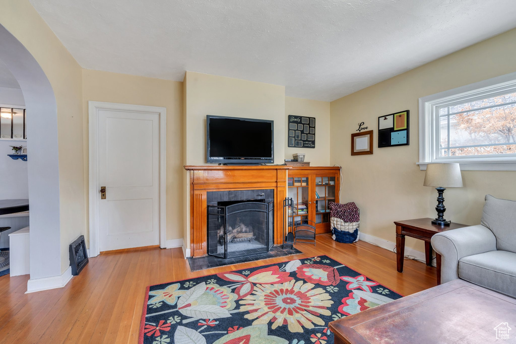 Living area featuring a tiled fireplace, arched walkways, baseboards, and wood finished floors