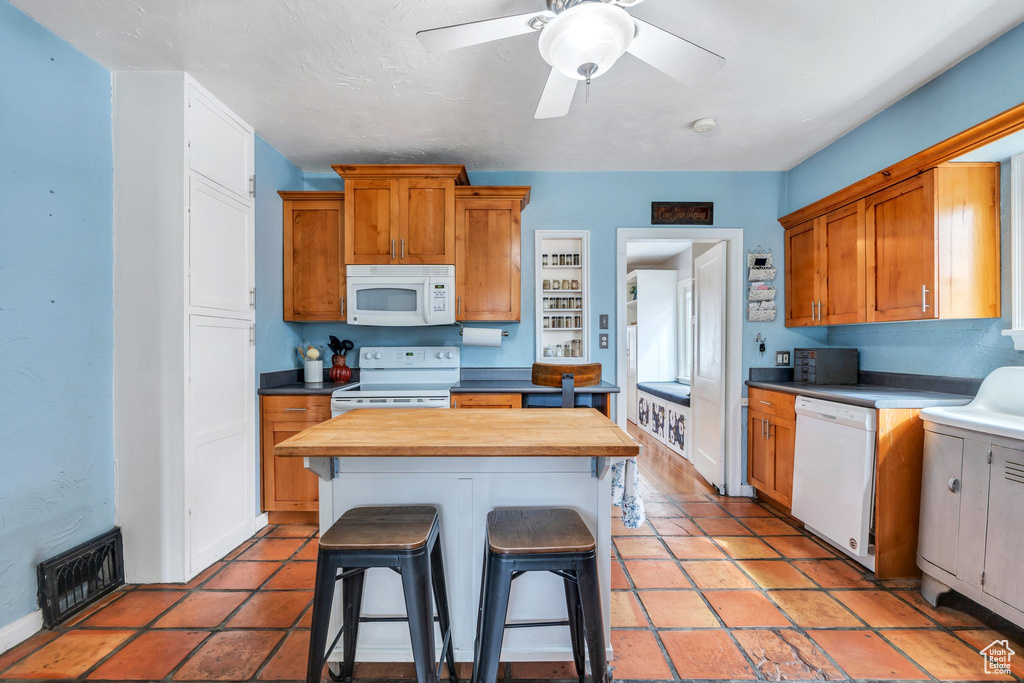 Kitchen with white appliances, a breakfast bar, a kitchen island, wood counters, and visible vents