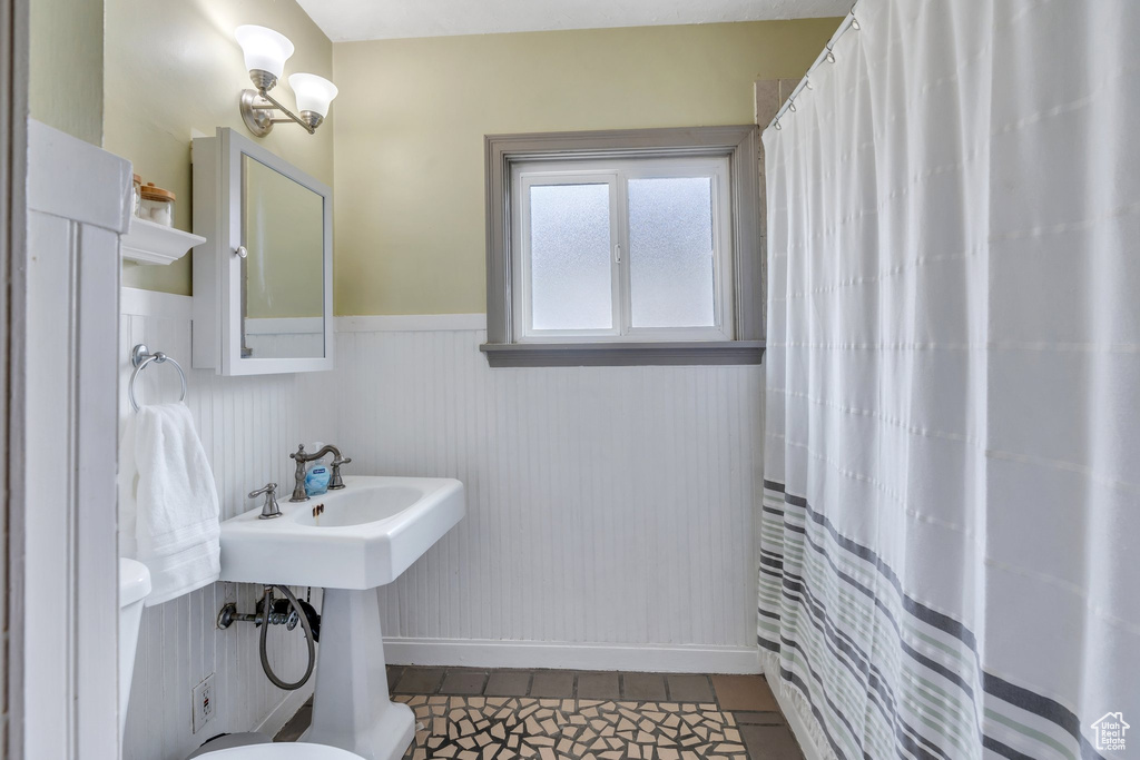 Bathroom with a wainscoted wall, toilet, tile patterned floors, and curtained shower