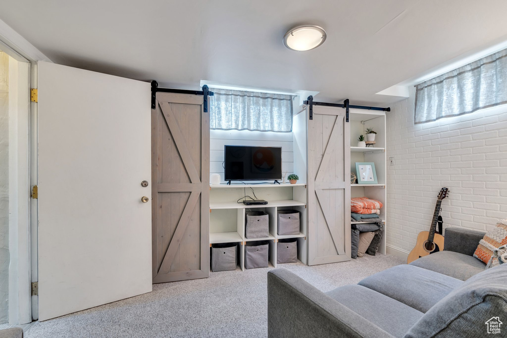 Carpeted living room with a barn door and brick wall