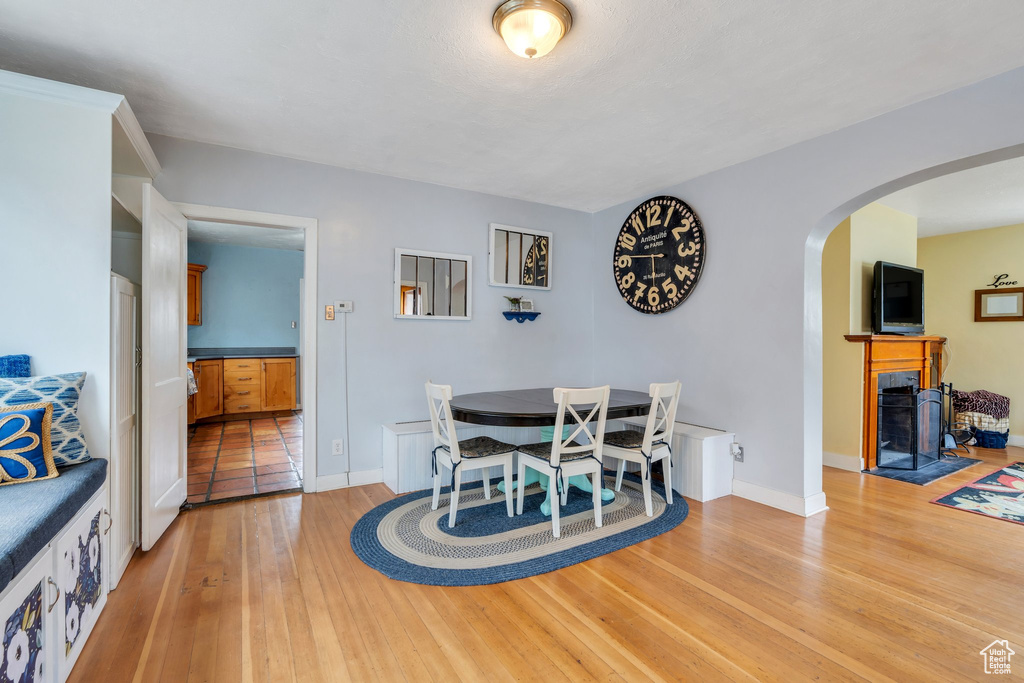 Dining space featuring light wood-style flooring, arched walkways, a fireplace with flush hearth, and baseboards