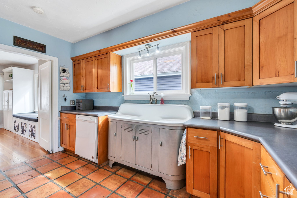 Kitchen with brown cabinets, white dishwasher, decorative backsplash, and a sink