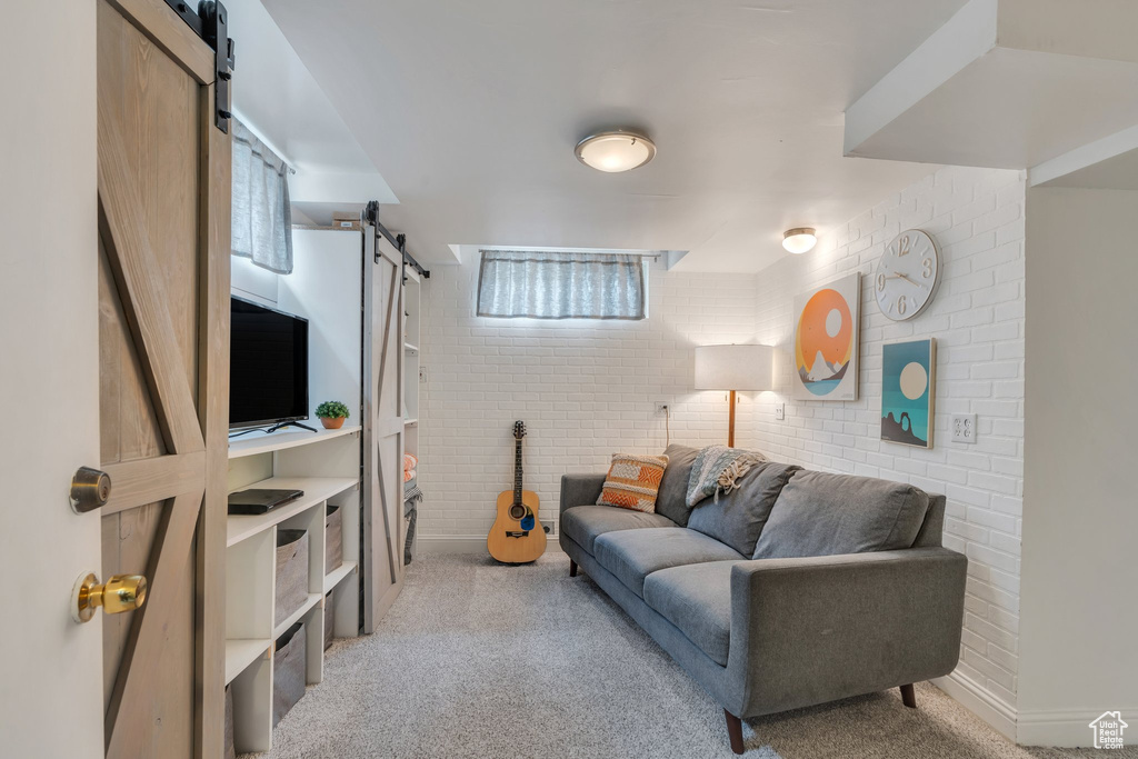Carpeted living room with brick wall, baseboards, and a barn door