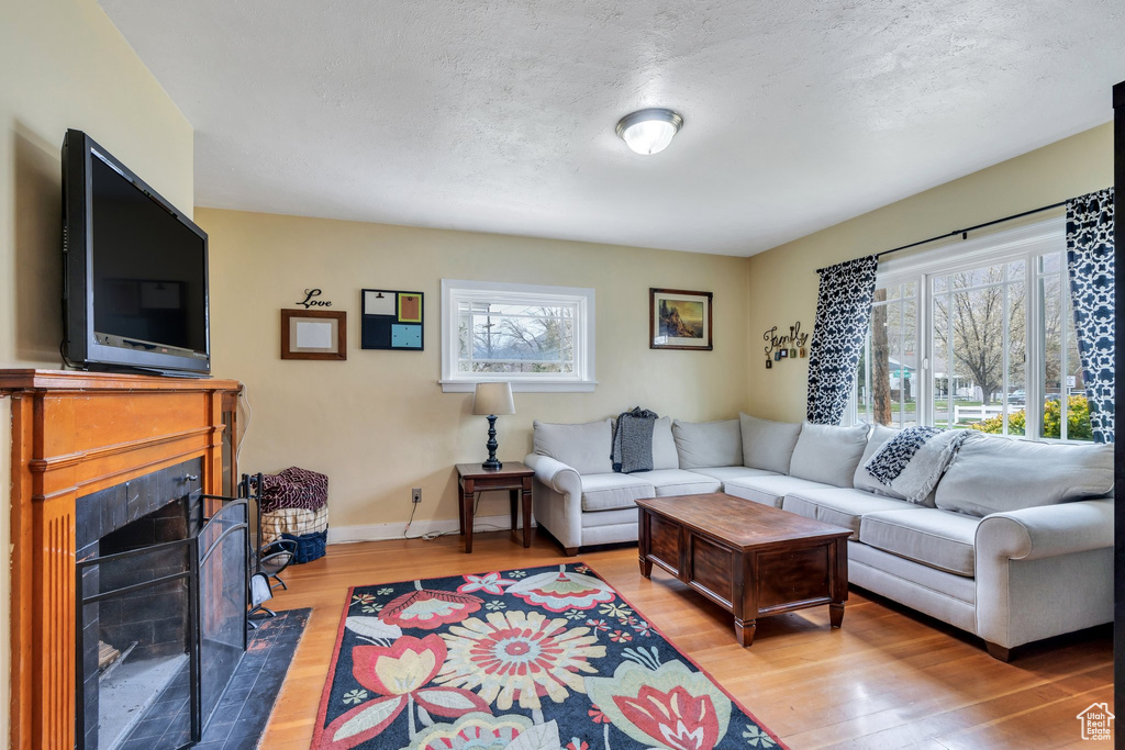 Living area featuring light wood finished floors, baseboards, a tile fireplace, and a textured ceiling