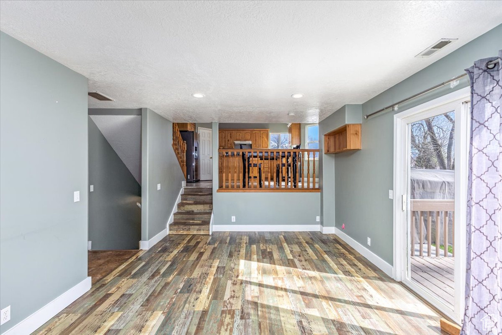 Unfurnished living room featuring a textured ceiling, visible vents, baseboards, wood finished floors, and stairway