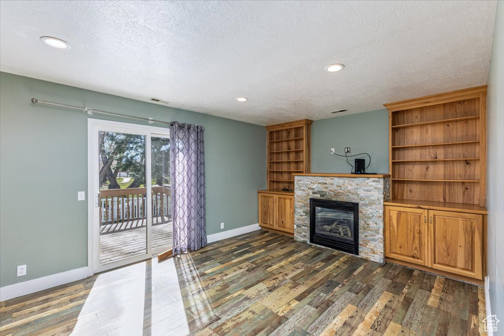 Unfurnished living room featuring dark wood finished floors, a stone fireplace, baseboards, and a textured ceiling