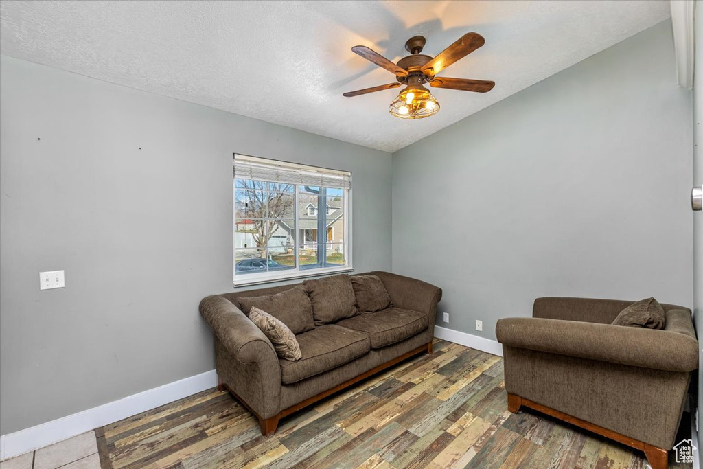 Living area with vaulted ceiling, baseboards, a textured ceiling, a ceiling fan, and wood finished floors