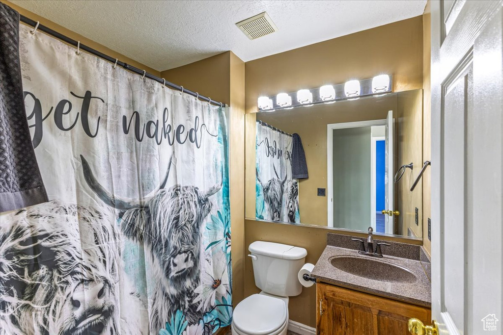 Bathroom featuring toilet, curtained shower, vanity, a textured ceiling, and visible vents