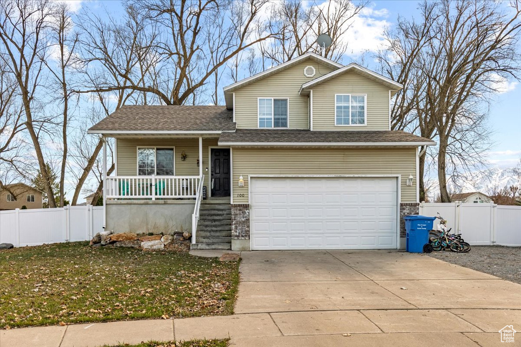 View of front of house with a gate, fence, a garage, concrete driveway, and a porch