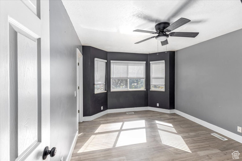 Empty room with a textured ceiling, visible vents, baseboards, wood finished floors, and a ceiling fan