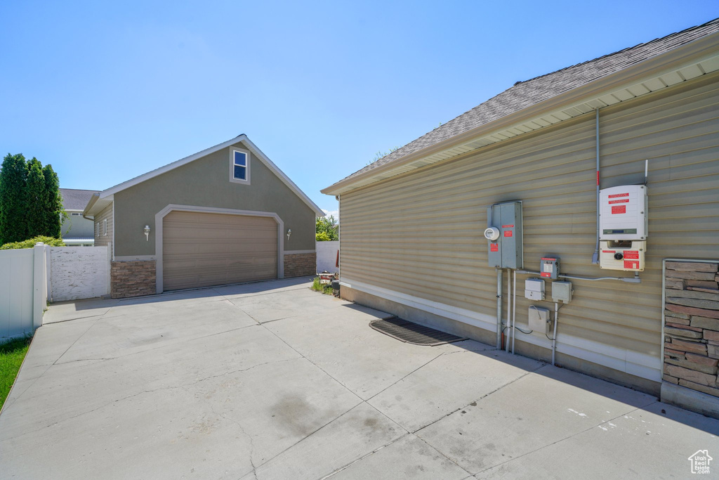 View of side of property with an outbuilding, a detached garage, fence, and a shingled roof