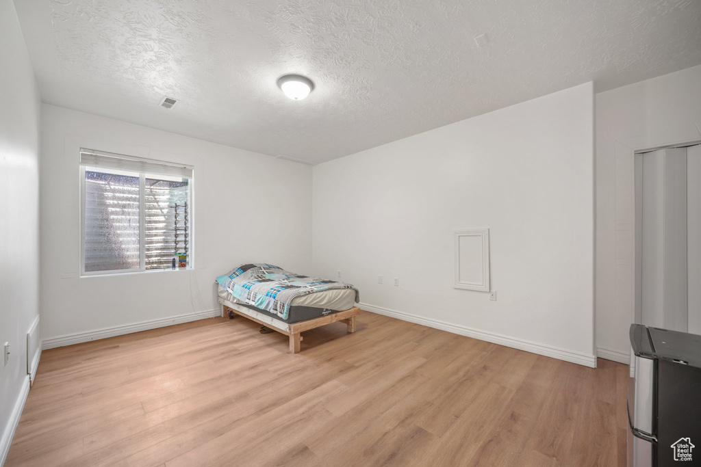 Bedroom with a textured ceiling, light wood-style flooring, and baseboards