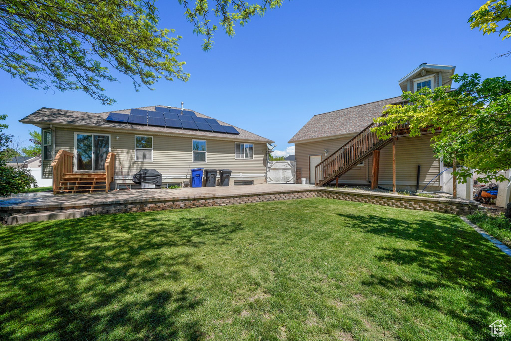 Back of house with stairs, solar panels, a yard, and a patio area