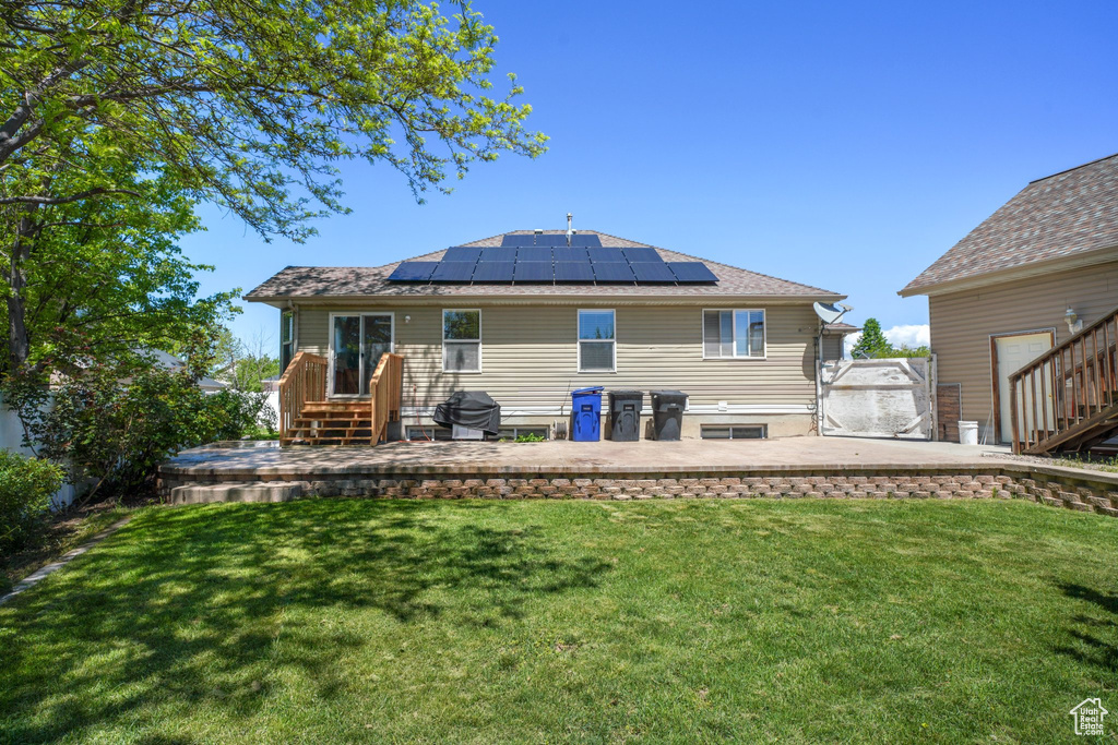 Rear view of property featuring solar panels, a lawn, and a patio area