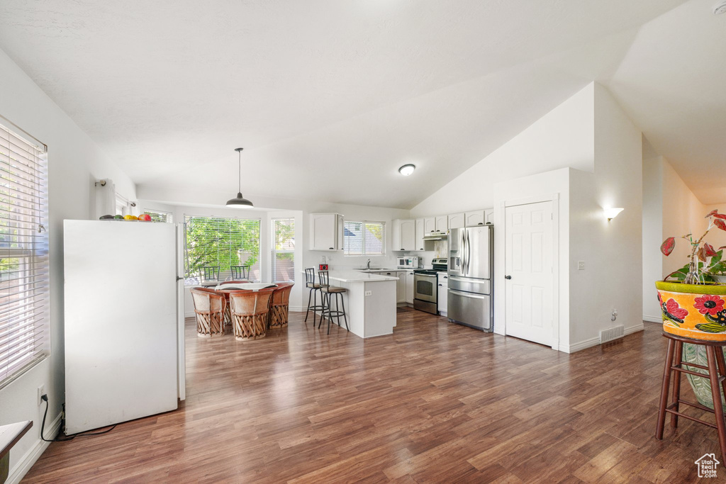 Kitchen with appliances with stainless steel finishes, white cabinets, a breakfast bar area, dark wood-style flooring, and light countertops