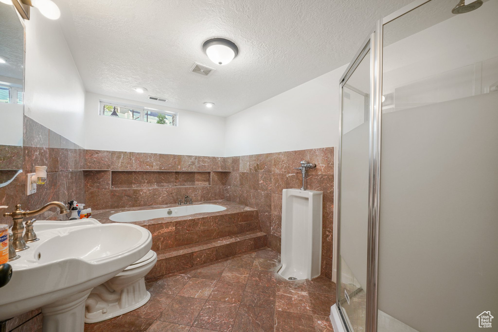 Bathroom with tile walls, a shower stall, a garden tub, a textured ceiling, and toilet