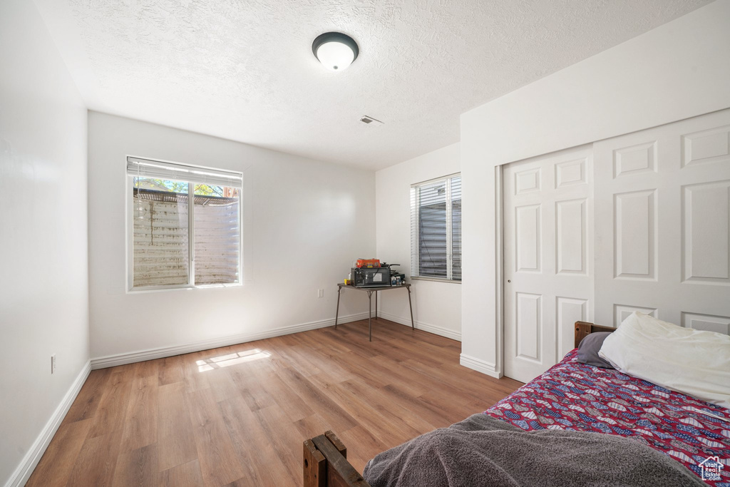 Bedroom with wood finished floors, a textured ceiling, baseboards, and a closet