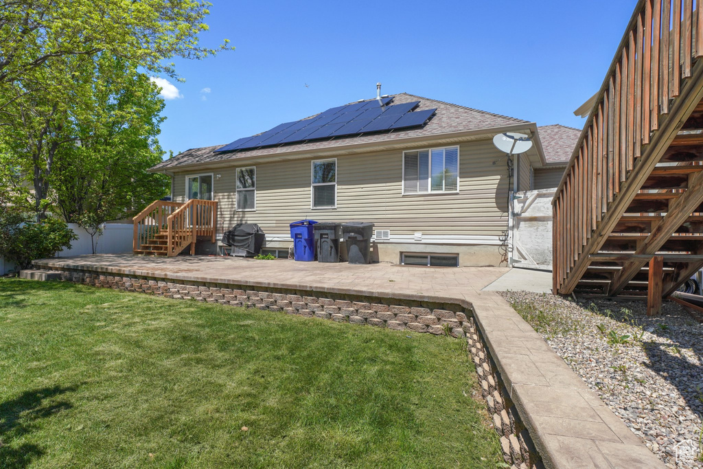 Back of property with solar panels, stairs, roof with shingles, and a patio area