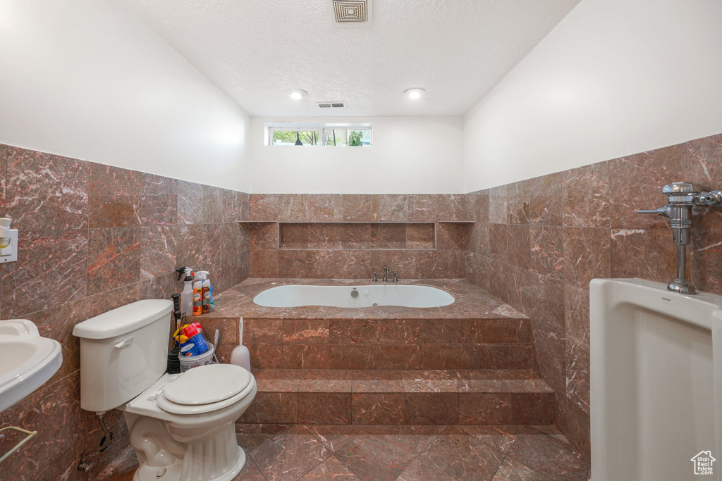Bathroom with tile walls, toilet, a bath, marble finish flooring, and a textured ceiling