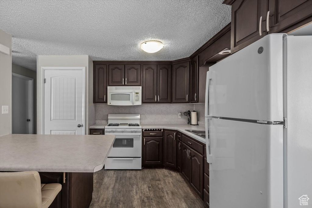 Kitchen featuring a textured ceiling, light countertops, white appliances, dark brown cabinets, and dark wood finished floors