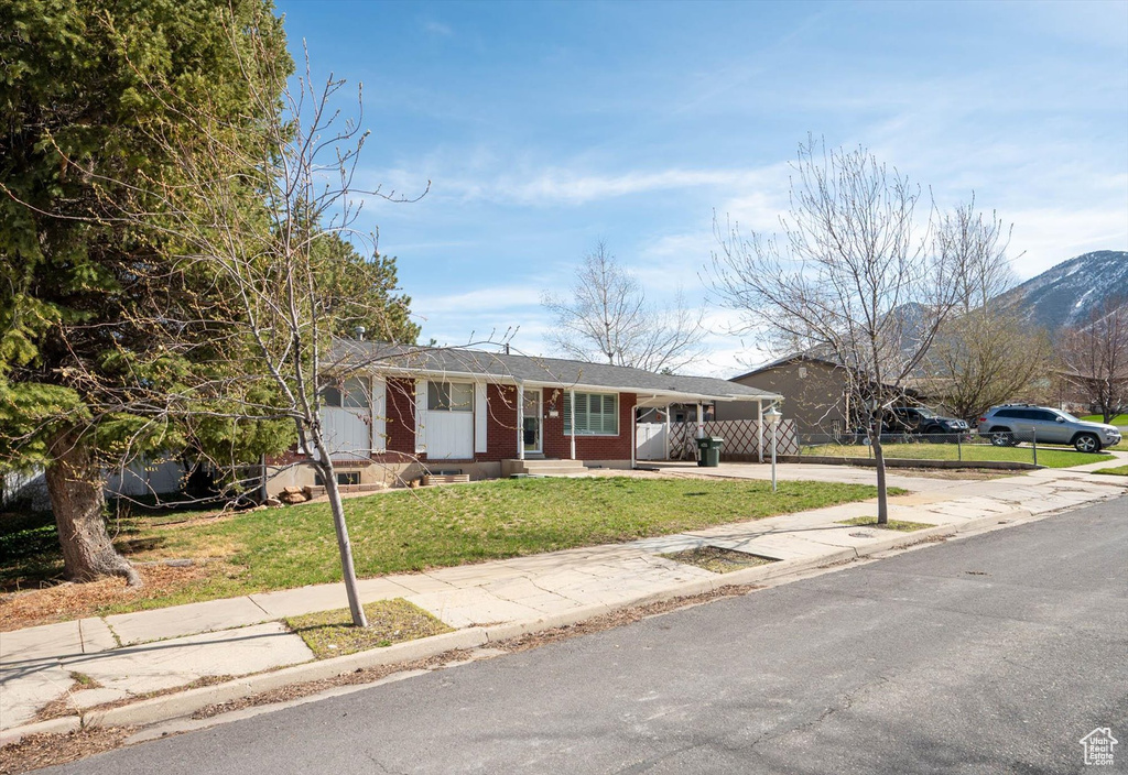 Single story home with concrete driveway, fence, a mountain view, a front lawn, and an attached carport