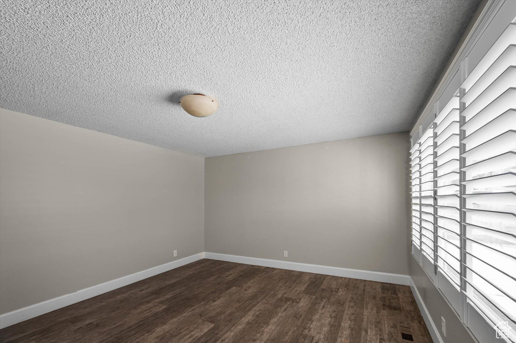 Unfurnished room featuring dark wood-type flooring, baseboards, and a textured ceiling