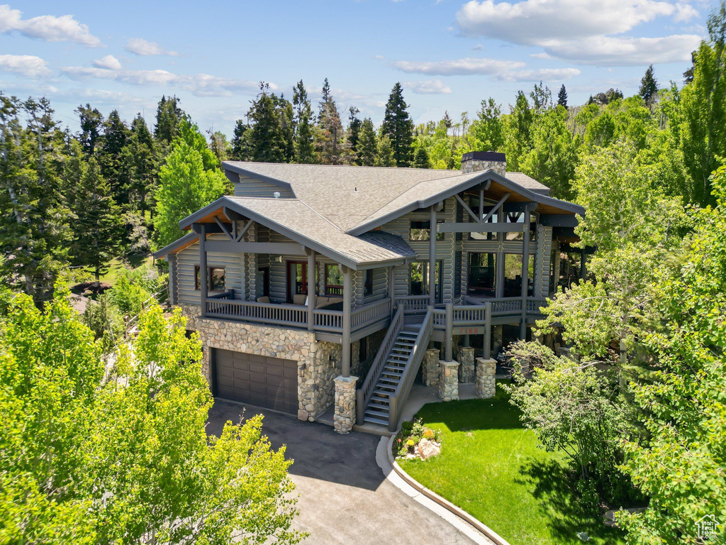 View of front facade featuring stone siding, asphalt driveway, a shingled roof, an attached garage, and a front lawn
