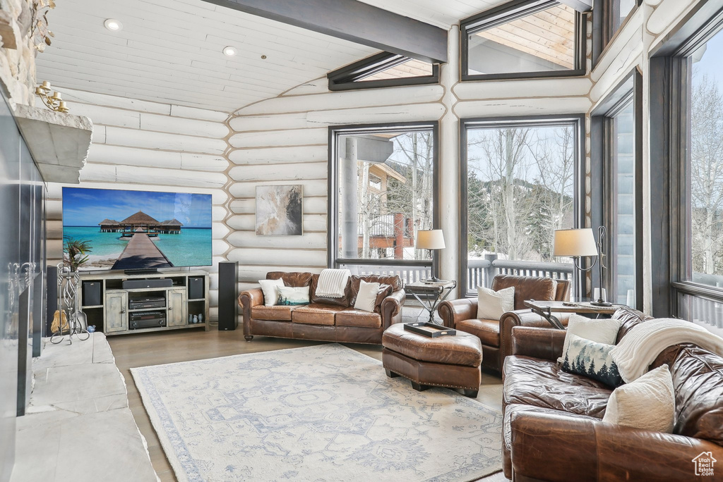 Living room with rustic walls, wood ceiling with exposed beams, high vaulted ceiling, and healthy amount of natural light