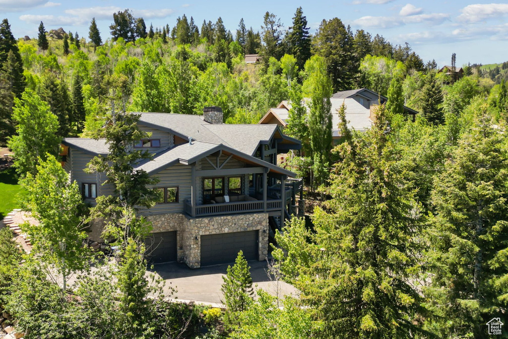 View of front of home with stone siding, an attached garage, concrete driveway, a chimney, and roof with shingles