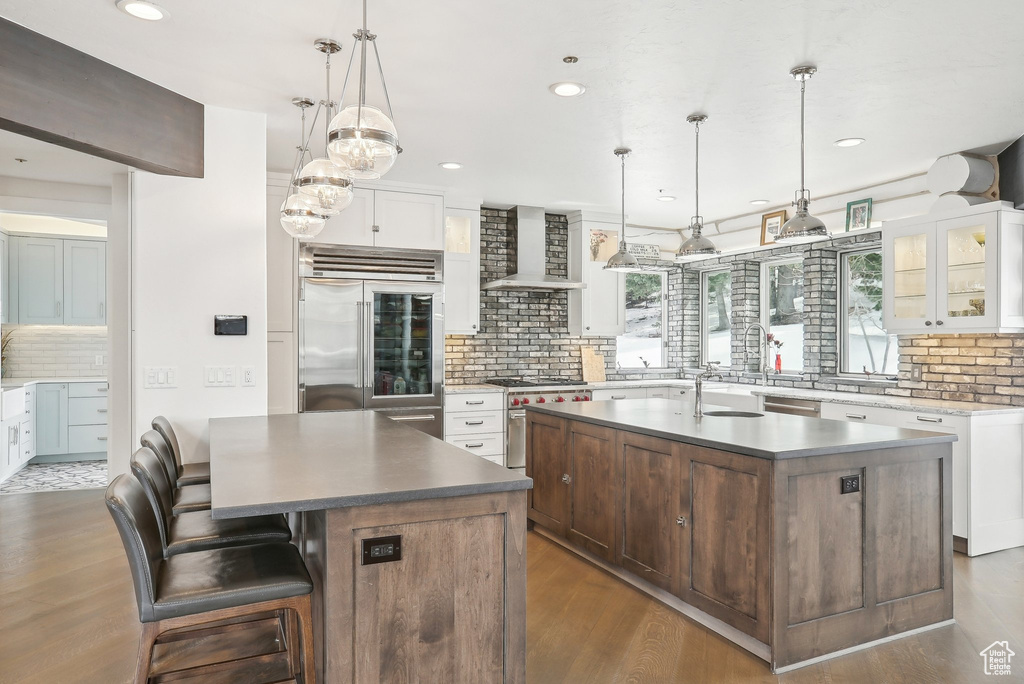 Kitchen with high end appliances, a center island with sink, backsplash, wall chimney range hood, and dark wood-style floors