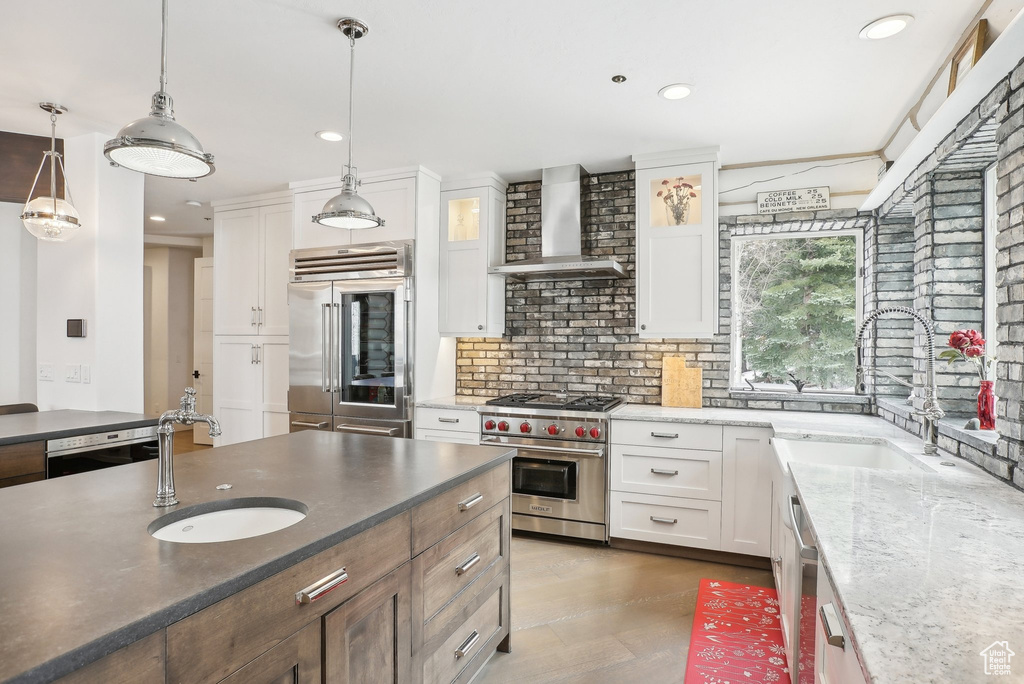 Kitchen with wall chimney range hood, premium appliances, a sink, recessed lighting, and white cabinets