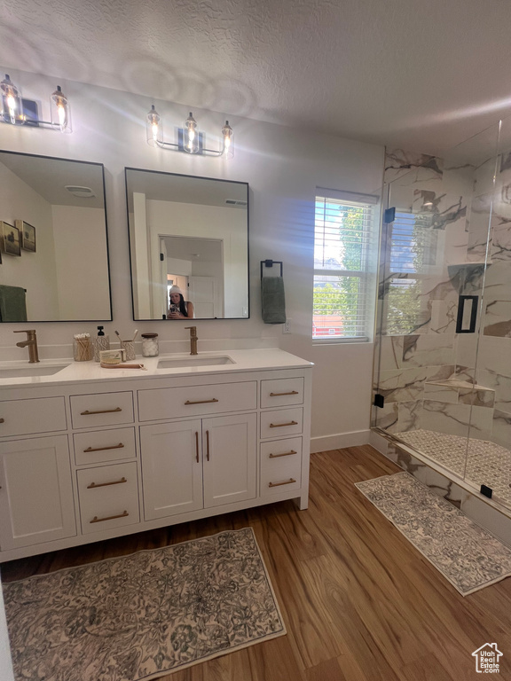 Bathroom with a marble finish shower, wood finished floors, double vanity, baseboards, and a textured ceiling