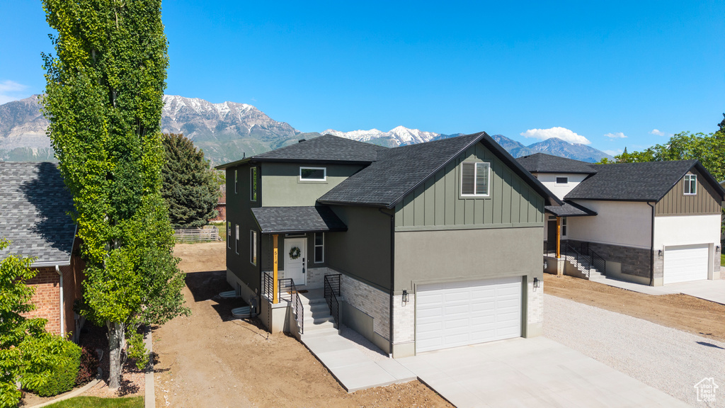 View of front of house featuring a mountain view, concrete driveway, a shingled roof, board and batten siding, and stucco siding