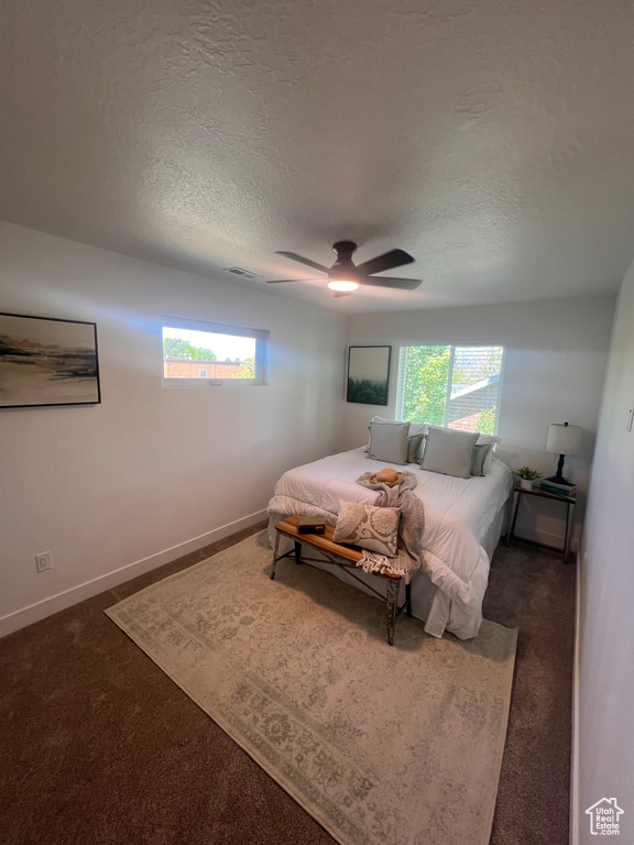 Bedroom with a textured ceiling, multiple windows, carpet floors, and ceiling fan