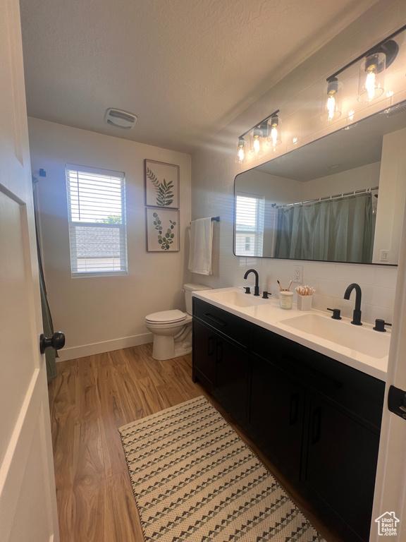 Full bath featuring double vanity, toilet, wood finished floors, a textured ceiling, and tasteful backsplash