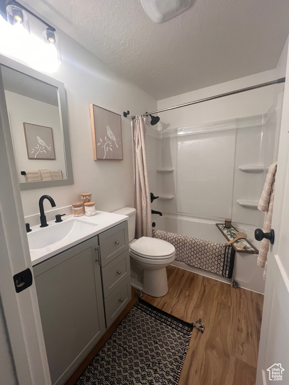 Bathroom with wood finished floors, vanity, toilet, shower / bathtub combination with curtain, and a textured ceiling