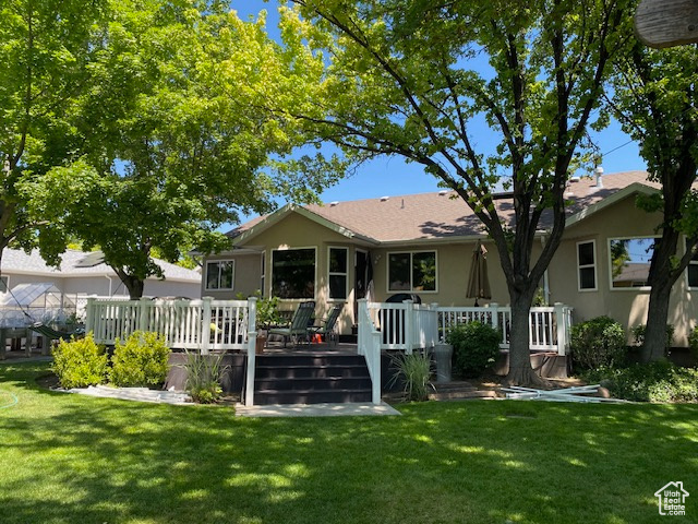 Back of property featuring a lawn, stucco siding, and a deck