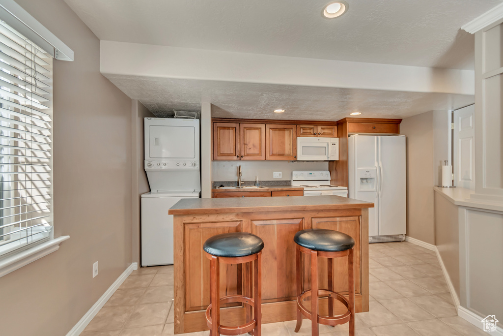 Kitchen featuring stacked washer / drying machine, a sink, a center island, white appliances, and recessed lighting