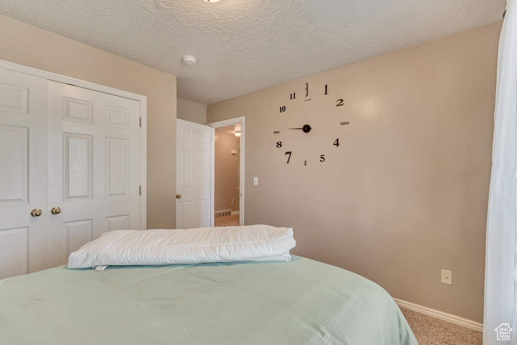 Carpeted bedroom featuring baseboards, a textured ceiling, visible vents, and a closet