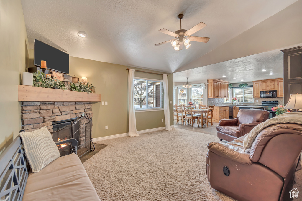 Living area featuring baseboards, a ceiling fan, a stone fireplace, light carpet, and lofted ceiling
