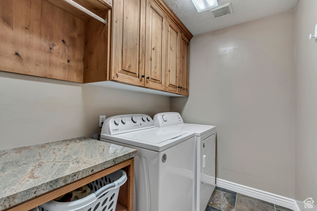 Washroom featuring washing machine and clothes dryer, a textured ceiling, visible vents, baseboards, and cabinet space