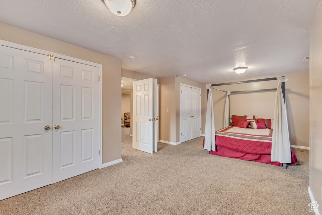 Bedroom featuring baseboards, multiple closets, a textured ceiling, and carpet