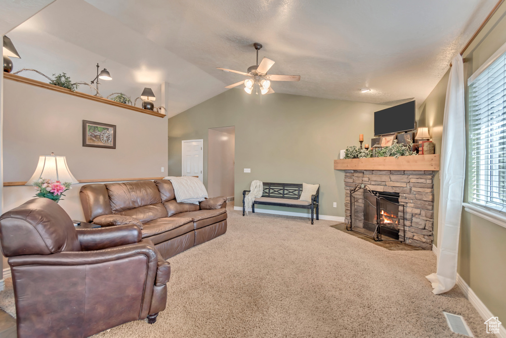Carpeted living room featuring vaulted ceiling, baseboards, visible vents, a ceiling fan, and a fireplace