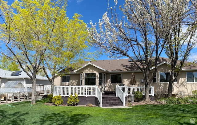 Rear view of property featuring stucco siding, a yard, and a wooden deck