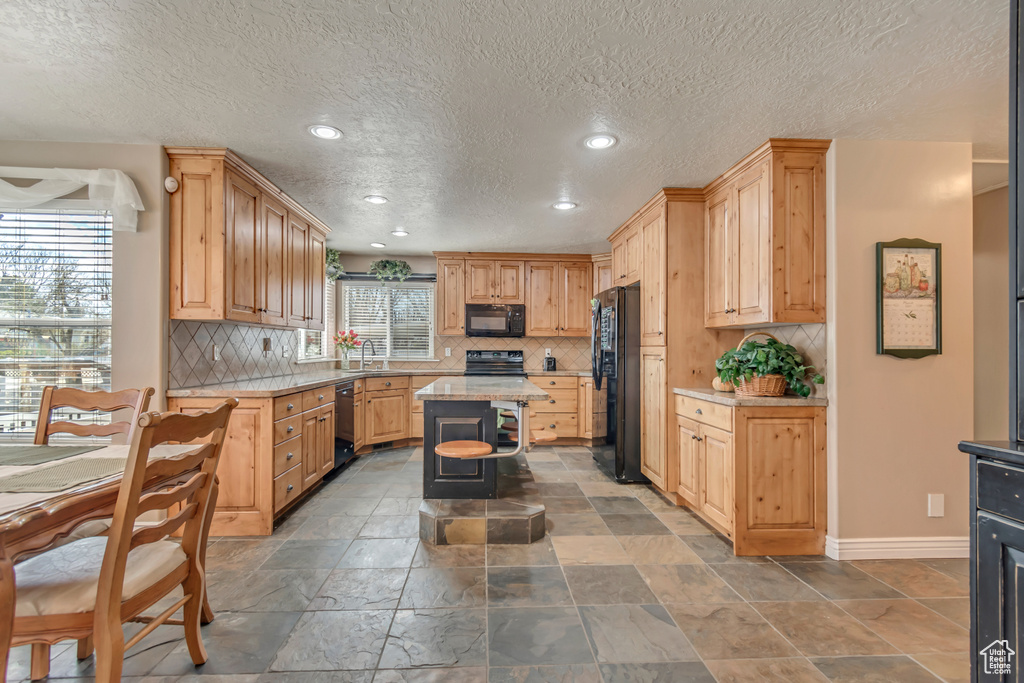 Kitchen featuring light countertops, tasteful backsplash, baseboards, a sink, and black appliances