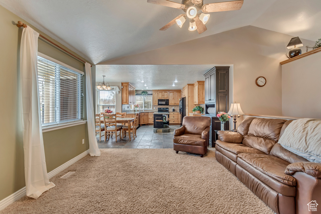 Living room with light carpet, ceiling fan with notable chandelier, lofted ceiling, and baseboards