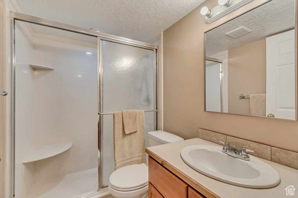 Full bathroom with a textured ceiling, visible vents, toilet, vanity, and a stall shower
