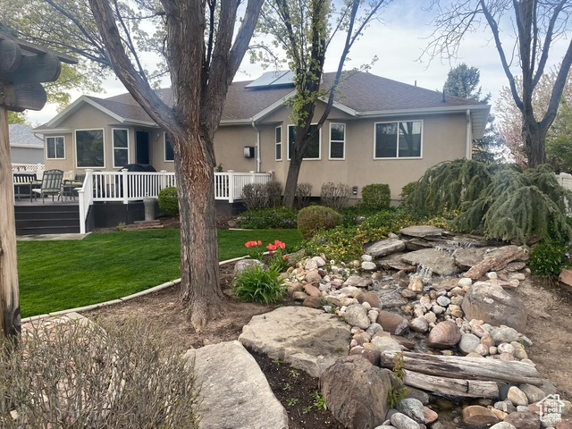 View of front of house featuring stucco siding, roof with shingles, solar panels, and a front yard